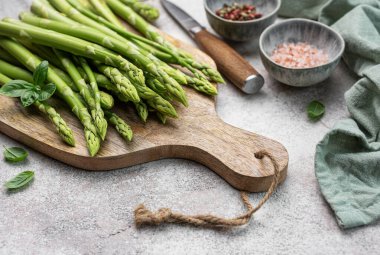 Bir grup çiğ kuşkonmaz, gri beton arka planda farklı baharatlar içerir.