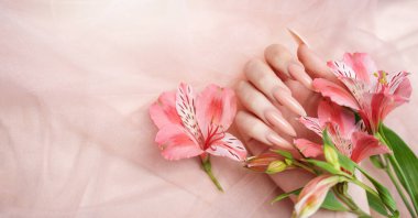 Zarif pastel pembe doğal manikür. Pembe ipek arka planda çiçekli kadın elleri..