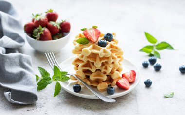 Beton gri arka planda çilek ve yaban mersinli taze pişmiş waffle. Ev yapımı pişirme..