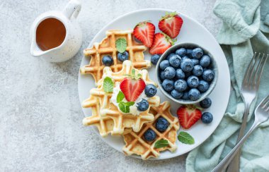 Beton gri arka planda çilek ve yaban mersinli taze pişmiş waffle. Ev yapımı pişirme..