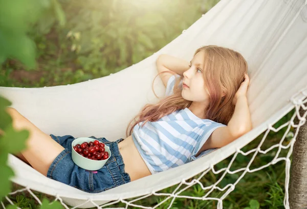 一个小女孩在吊床上休息 夏天吃樱桃 夏天在村子里 免版税图库照片