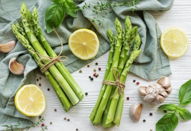 Bir grup çiğ kuşkonmaz beyaz ahşap arka planda farklı baharatlar içerir.
