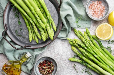 Bir grup çiğ kuşkonmaz, gri beton arka planda farklı baharatlar içerir.
