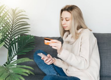 Akıllı telefon ve bankacılık kredi kartı tutan genç bir kadın, evde internet üzerinden alışveriş yapan mutlu bir kadın, internet mağazasından mal veya hizmet satın alan mutlu bir kadın..
