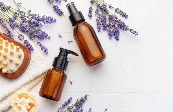 Lavender spa. Lavender salt, natural essential oil, massage brushes and fresh lavender on a white tile background.