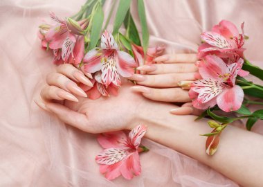 Zarif pastel pembe doğal manikür. Pembe ipek arka planda çiçekli kadın elleri..