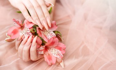 Zarif pastel pembe doğal manikür. Pembe ipek arka planda çiçekli kadın elleri..