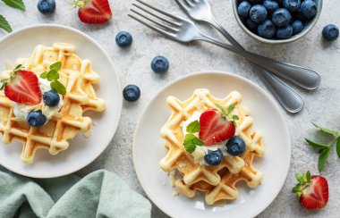 Beton gri arka planda çilek ve yaban mersinli taze pişmiş waffle. Ev yapımı pişirme..