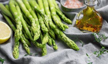 Bir grup çiğ kuşkonmaz, gri beton arka planda farklı baharatlar içerir.