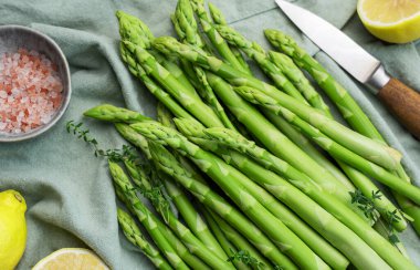 Bir grup çiğ kuşkonmaz, gri beton arka planda farklı baharatlar içerir.