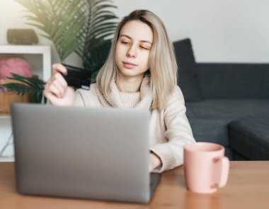 Kredi kartı tutan ve dizüstü bilgisayar kullanan genç bir kadın. İnternette çalışan bir kız. Çevrimiçi alışveriş, internet bankacılığı, evden çalışma 