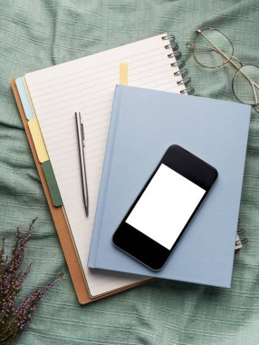 Ofis malzemelerinin üst görüntüsü, boş ekranlı akıllı telefon, defterler, kalemler, gözlükler...