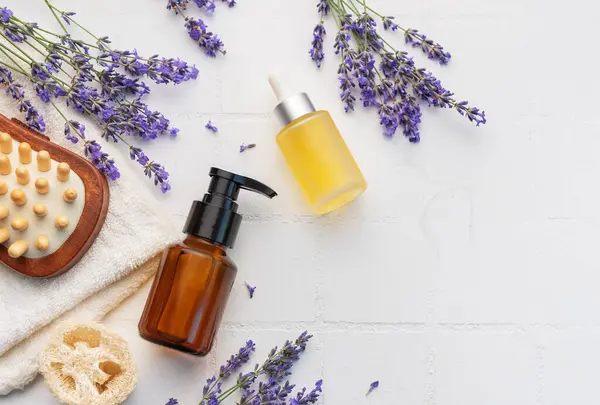 Lavender spa. Lavender salt, natural essential oil, massage brushes and fresh lavender on a white tile background.