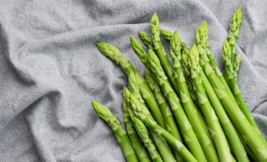 Gri tekstil arka planında taze yeşil kuşkonmaz. Düz yatıyordu