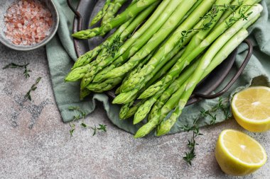 Bir grup çiğ kuşkonmaz, gri beton arka planda farklı baharatlar içerir.