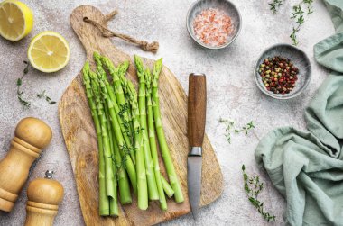 Bir grup çiğ kuşkonmaz, gri beton arka planda farklı baharatlar içerir.