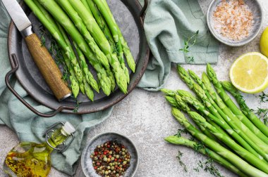 Bir grup çiğ kuşkonmaz, gri beton arka planda farklı baharatlar içerir.