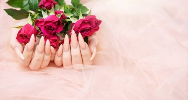 Zarif pastel pembe doğal manikür. Pembe ipek arka planda gülleri olan kadın elleri.