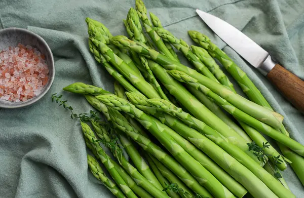 Bir grup çiğ kuşkonmaz, gri beton arka planda farklı baharatlar içerir.