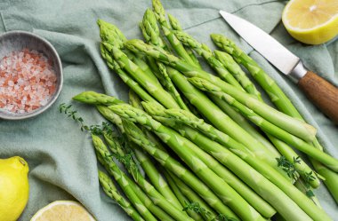 Bir grup çiğ kuşkonmaz, gri beton arka planda farklı baharatlar içerir.