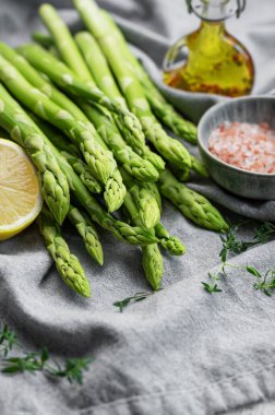 Bir grup çiğ kuşkonmaz, gri beton arka planda farklı baharatlar içerir.