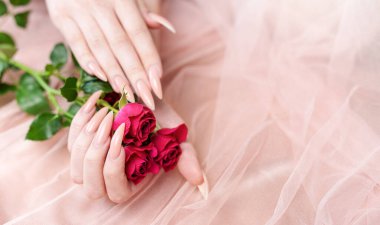 Zarif pastel pembe doğal manikür. Pembe ipek arka planda gülleri olan kadın elleri.