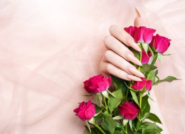 Zarif pastel pembe doğal manikür. Pembe ipek arka planda gülleri olan kadın elleri.