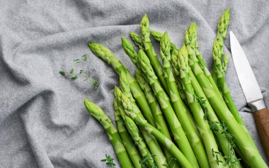 Gri tekstil arka planında taze yeşil kuşkonmaz. Düz yatıyordu