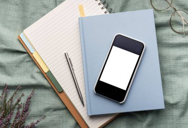 Ofis malzemelerinin üst görüntüsü, boş ekranlı akıllı telefon, defterler, kalemler, gözlükler...