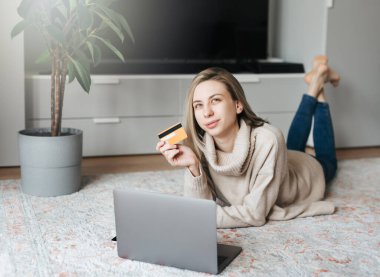 Kredi kartı tutan ve dizüstü bilgisayar kullanan genç bir kadın. İnternette çalışan bir kız. Çevrimiçi alışveriş, internet bankacılığı, evden çalışma 