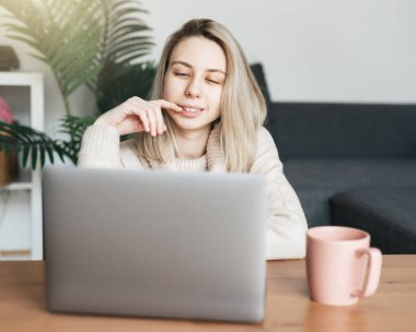 Evde dizüstü bilgisayar kullanan genç bir kadın oturma odasında rahat bir şekilde oturuyor.. 