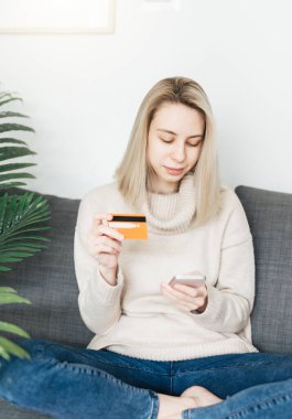 Akıllı telefon ve bankacılık kredi kartı tutan genç bir kadın, evde internet üzerinden alışveriş yapan mutlu bir kadın, internet mağazasından mal veya hizmet satın alan mutlu bir kadın..