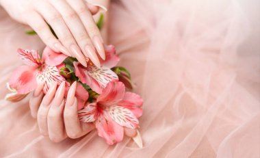 Zarif pastel pembe doğal manikür. Pembe ipek arka planda çiçekli kadın elleri..