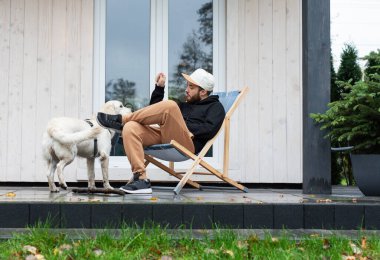 Genç bir adam bir golden retriever ile kır evinin yakınında dinleniyor.. 