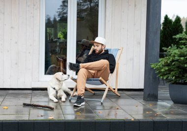 Genç bir adam bir golden retriever ile kır evinin yakınında dinleniyor.. 