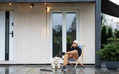 Genç adam Golden Retriever ile terasta oturuyor.