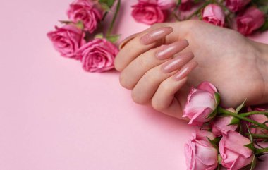 Güzel manikürlü kadın elleri ve pembe arka planda güller.