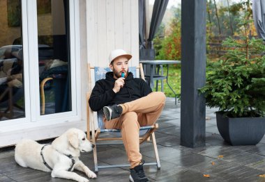 Genç adam Golden Retriever ile terasta oturuyor.