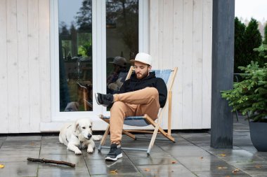 Genç adam Golden Retriever ile terasta oturuyor.