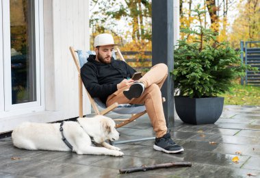Genç adam Golden Retriever ile terasta oturuyor.