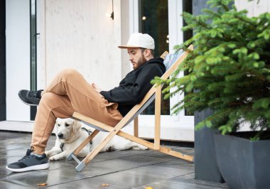 Genç adam Golden Retriever ile terasta oturuyor.