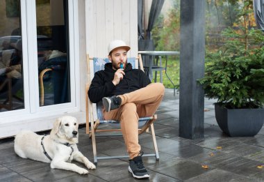 Genç adam Golden Retriever ile terasta oturuyor.