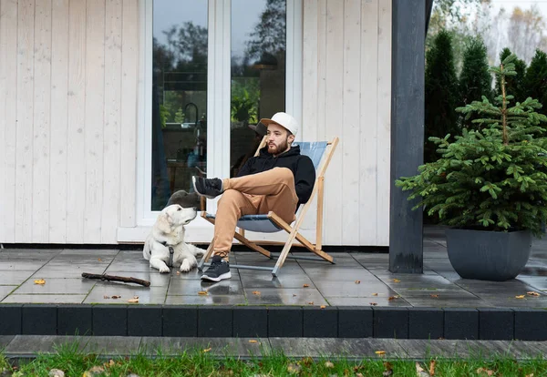 Genç adam Golden Retriever ile terasta oturuyor.
