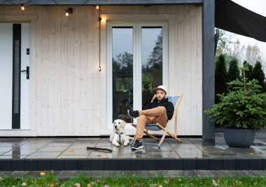 Genç adam Golden Retriever ile terasta oturuyor.