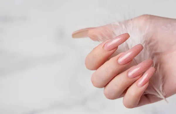粉红指甲设计的女手拿着一根羽毛 大理石背景上的粉色指甲油修指甲 图库图片