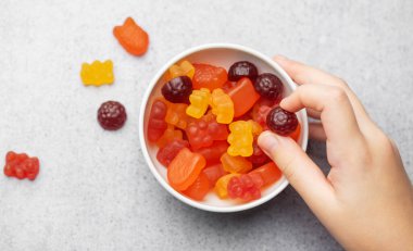 Çiğnenebilir jelibon, vitamin ve takviyeler. Bir kız elinde bir ayı vitamini tutuyor.. 
