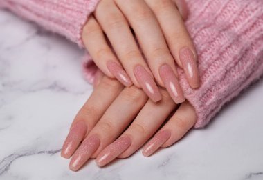 Pembe tırnak desenli kadın elleri. Mermer arka planda pembe oje manikürü. 