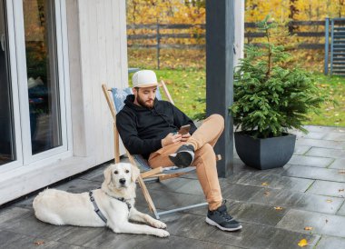 Genç adam Golden Retriever ile terasta oturuyor.