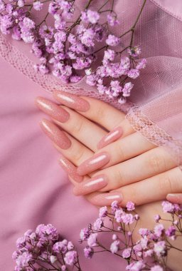 Güzel manikürlü, pembe ipekli çingene çiçekli kadın elleri.