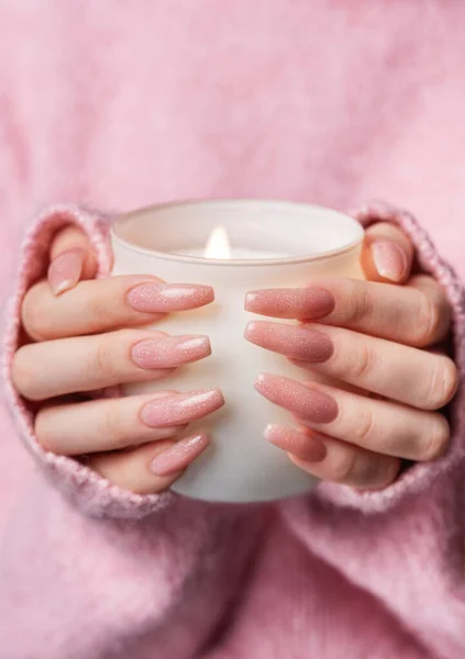 Young woman in a pink sweater with a pink manicure holds a  candle